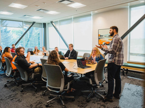 a person standing in front of a group of people around a table